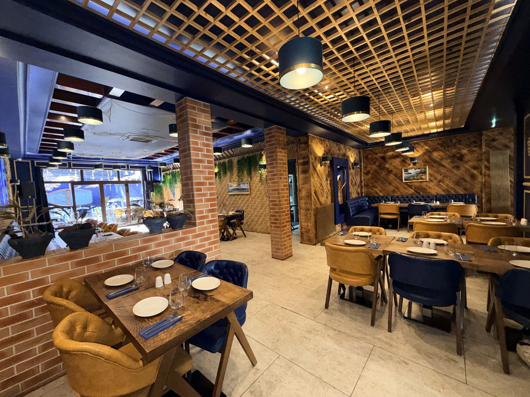 La salle du restaurant avec ses piliers en brique, son plafond en bois et ses fauteuils jaunes et bleus